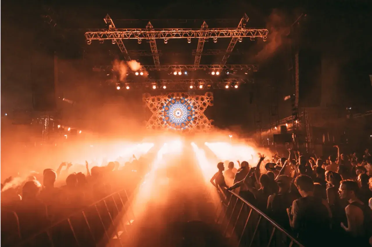 Foule en délire sous les lumières oranges d'une scène, un visuel psychédélique au centre. Photographie événementielle capturant l'énergie d'un concert.