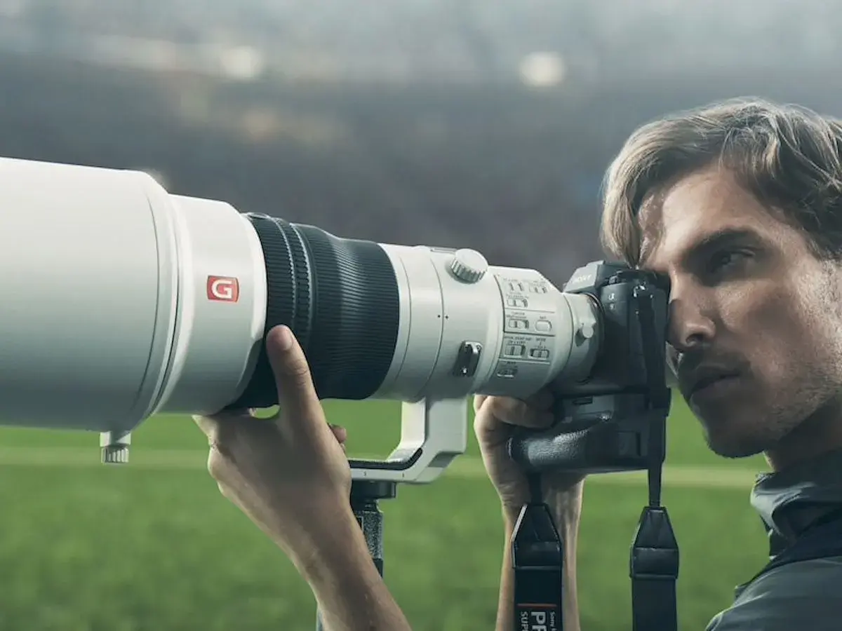 Photographe sportif utilisant un appareil photo Sony a9 II avec un téléobjectif blanc, prêt à capturer l'action sur le terrain.