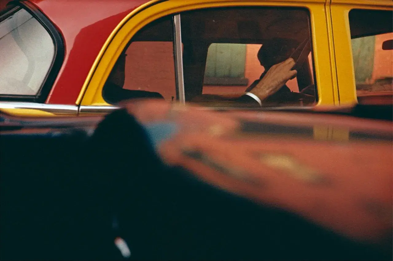 Vue à travers une fenêtre de voiture rouge et jaune, la main d'un homme au volant, typique des saul leiter photos.