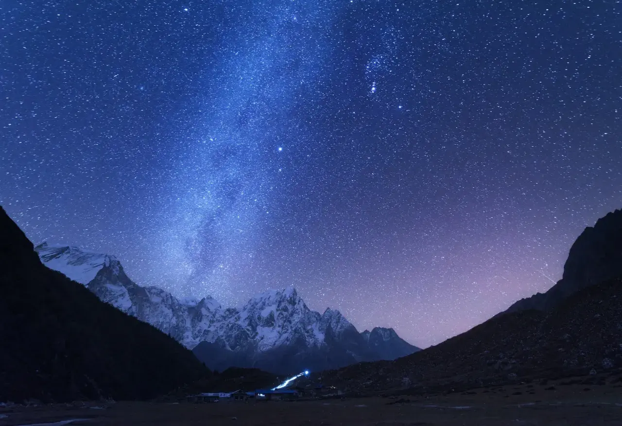 Magnifique photo de nuit. Le ciel étoilé scintille au-dessus de montagnes enneigées et d'un petit village illuminé.