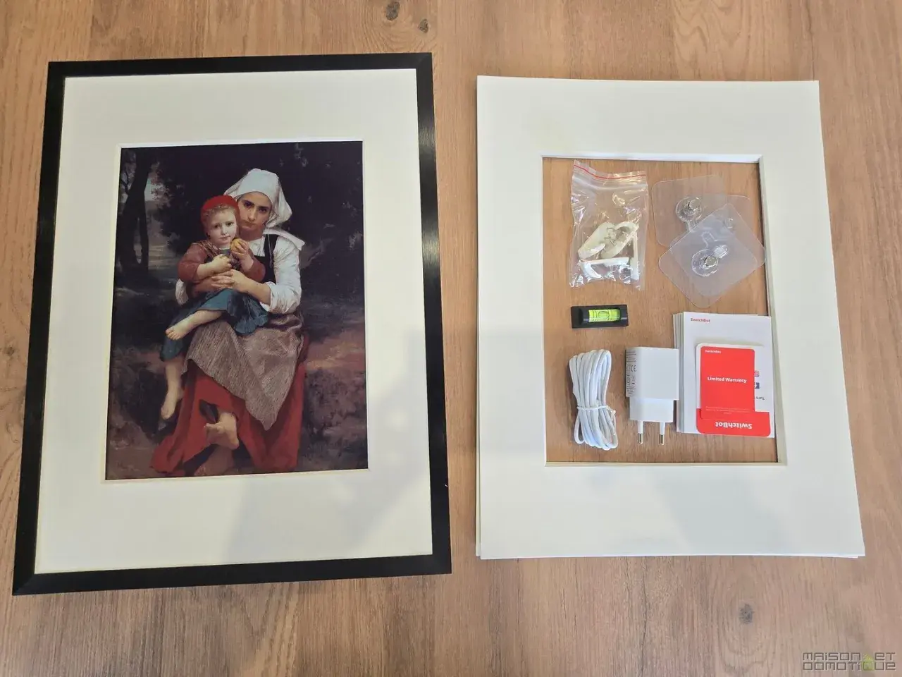 Cadre noir avec une peinture de mère et enfant, à côté d'un cadre blanc contenant des accessoires de montage, comme un niveau à bulle, un chargeur et des adhésifs, rappelant l'effet fresnel d'une œuvre d'art.