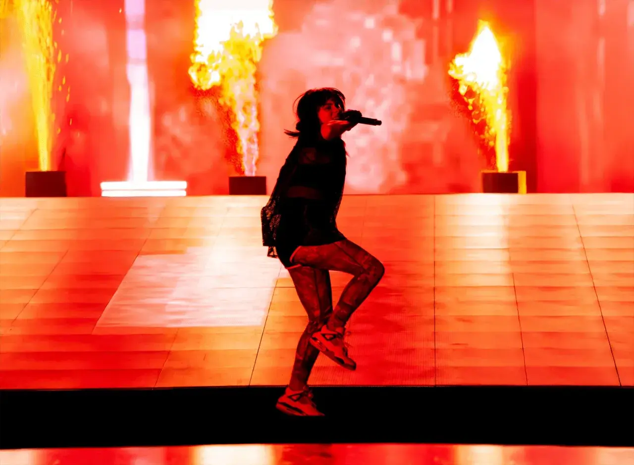Une artiste chante sur scène, entourée de flammes spectaculaires. Cette photo de concert capture l'énergie d'un spectacle enflammé.