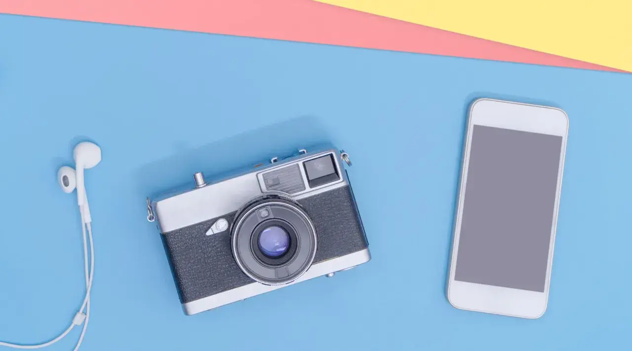 Un smartphone et un appareil photo argentique vintage côte à côte, avec des écouteurs blancs.