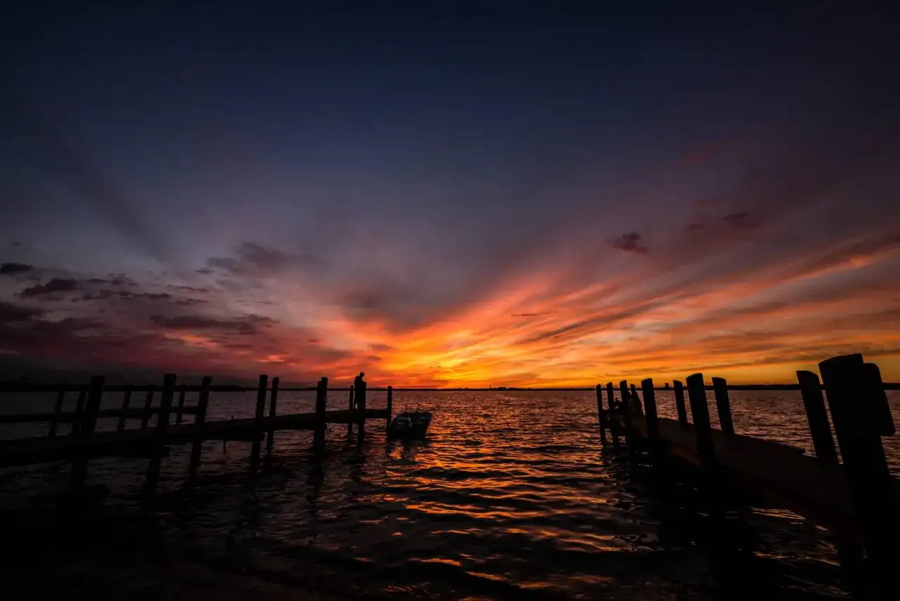 Magnifique photo coucher de soleil sur l'eau, avec des quais en silhouette et un ciel aux couleurs flamboyantes.