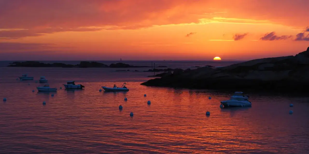Magnifique photo coucher de soleil sur la mer, avec des bateaux au mouillage et des rochers sombres.