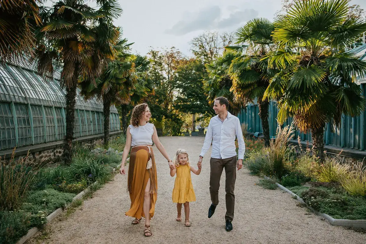 Aur&eacute;lie Ferrer et sa famille profitent d'une promenade ensoleill&eacute;e pr&egrave;s de serres, entour&eacute;s de palmiers luxuriants.
