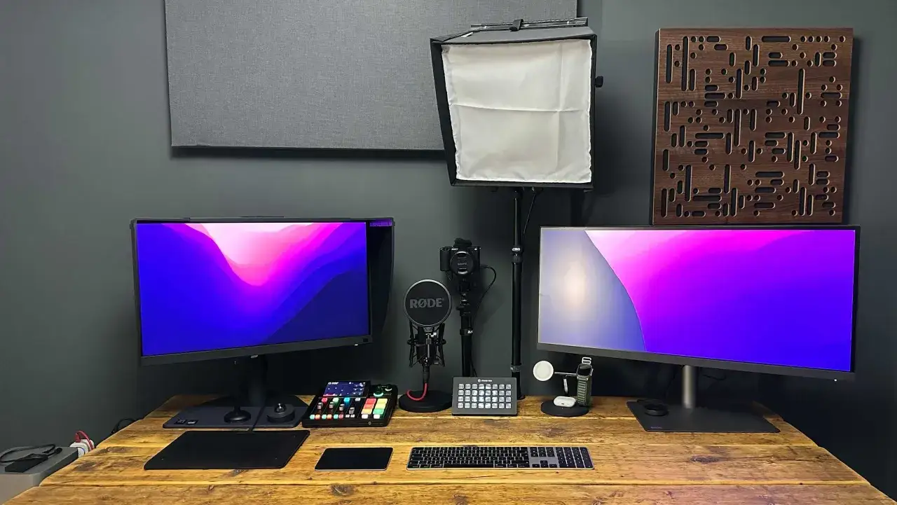 Postes de travail pour retouche photo : deux écrans, un micro Rode, une caméra, un clavier et une tablette graphique sur un bureau en bois.