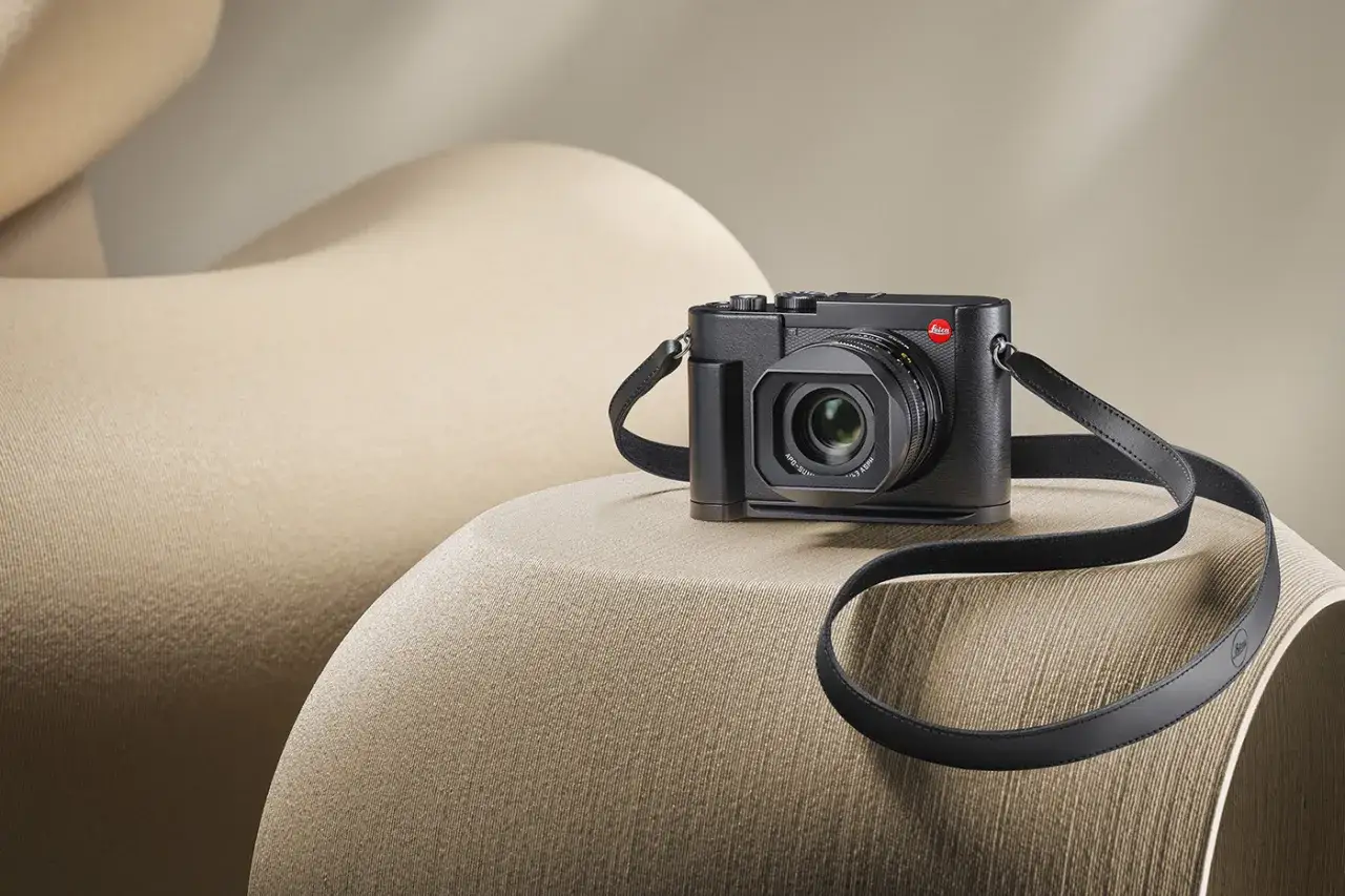 Un Leica Q3 noir, pr&ecirc;t pour un test, repose sur un fauteuil beige aux formes douces.