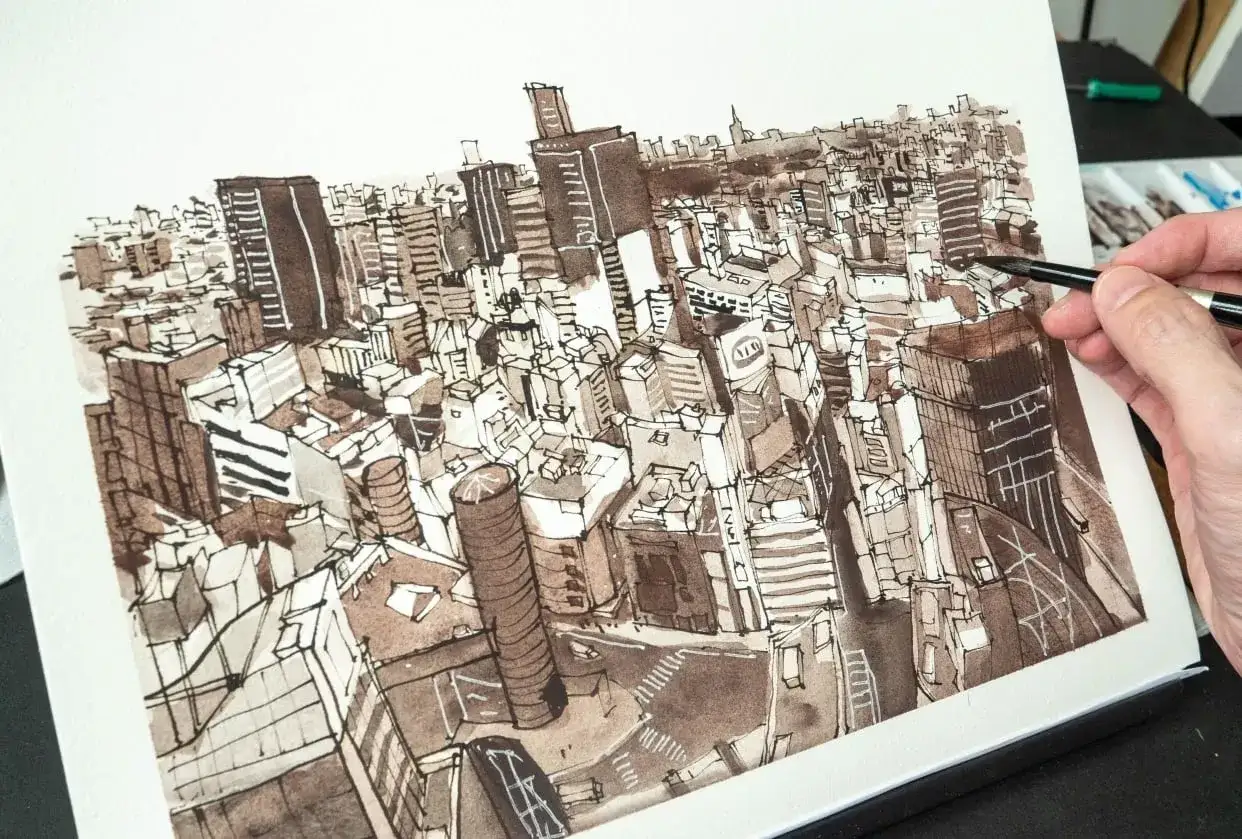 Vue aérienne d'une ville dessinée à l'encre, avec des gratte-ciel denses. Au premier plan, une main tient un pinceau, ajoutant des détails à l'œuvre.
