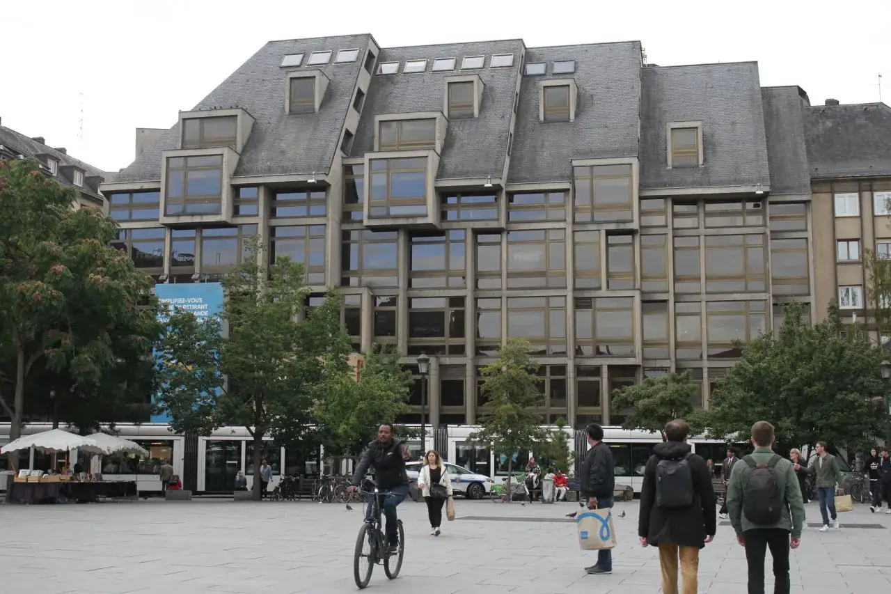 Une sc&egrave;ne anim&eacute;e &agrave; Strasbourg, avec un tramway, des passants et un b&acirc;timent moderne aux multiples fen&ecirc;tres. Spot photo Strasbourg.