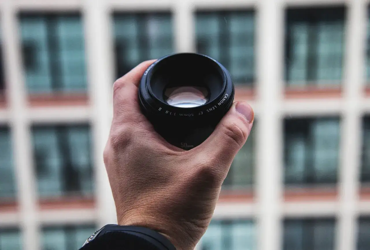 Une main tient un objectif Canon EF 50mm f/1.8 II. Cet objectif 50 mm pour quel usage ? Id&eacute;al pour les portraits et la photographie de rue.