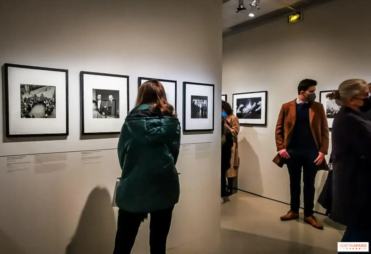 Visiteurs admirant des photographies en noir et blanc dans une galerie, peut-&ecirc;tre une exposition d'une photographe femme connue.