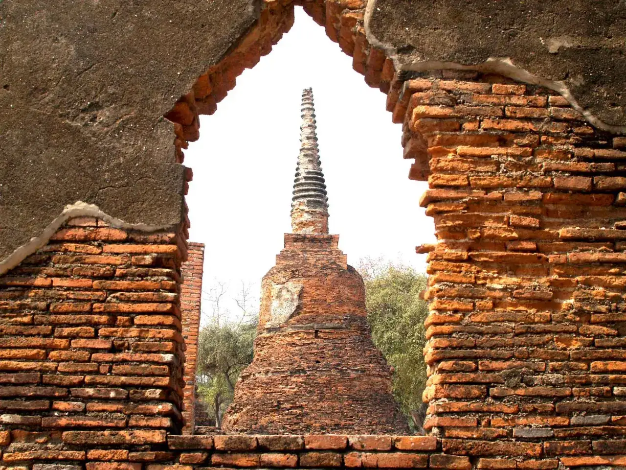 Ruines de briques rouges encadrant une pagode effilée sur fond blanc.