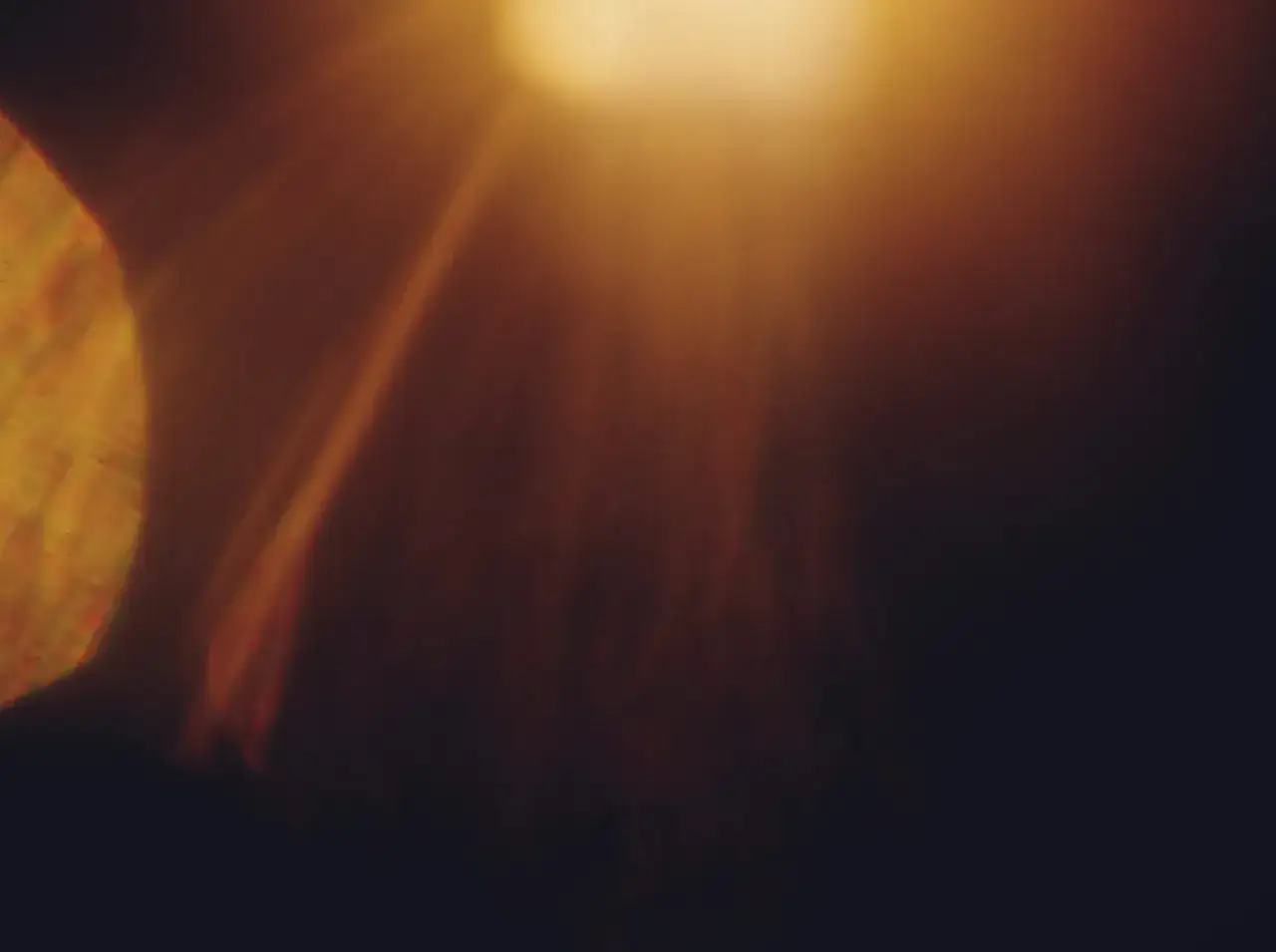 Un &eacute;clat de lumi&egrave;re dor&eacute; traverse un fond sombre, cr&eacute;ant un effet de flare photo.