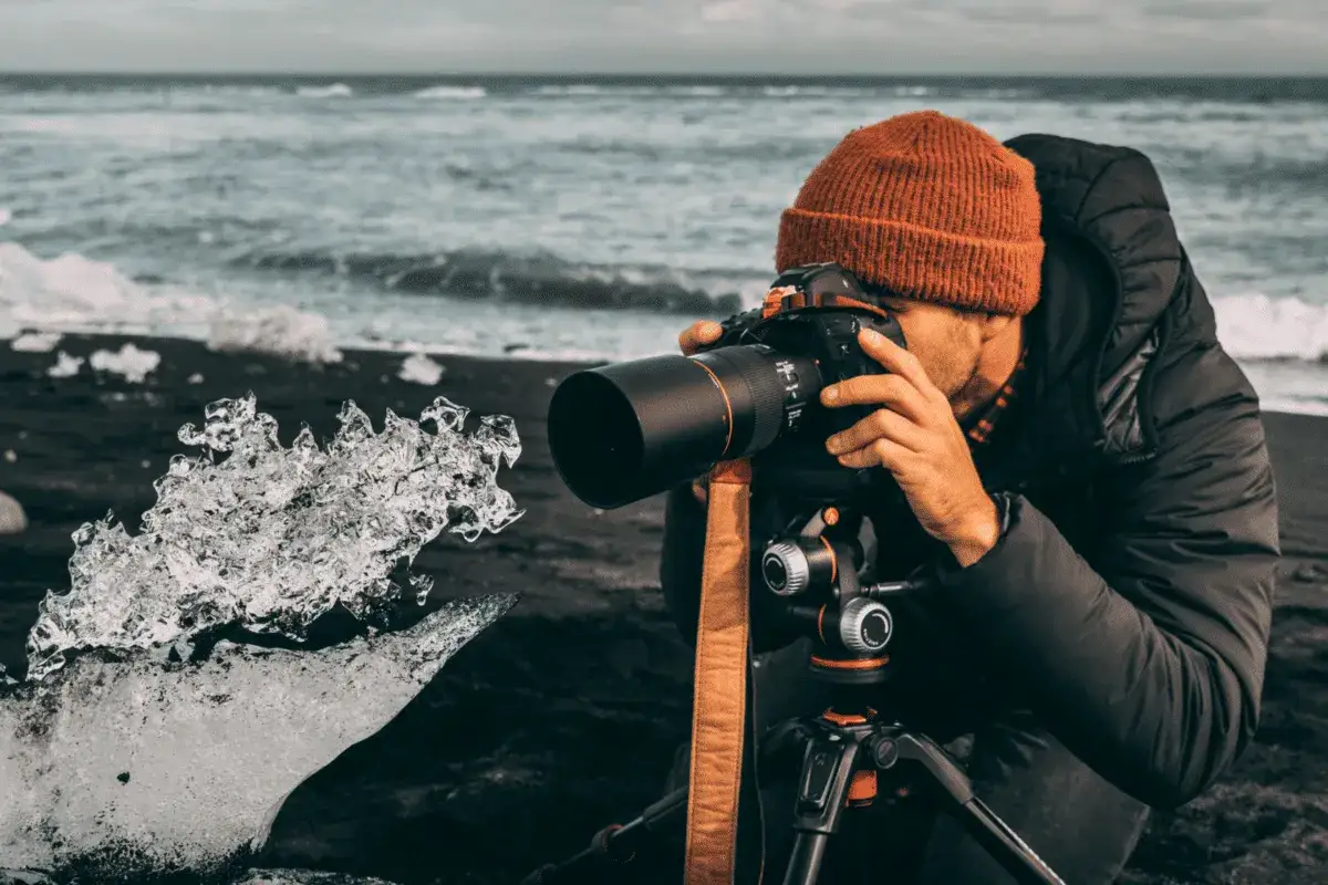 Photo macro d'un photographe capturant la beauté glacée d'un éclat de glace sur une plage de sable noir, avec l'océan en arrière-plan.