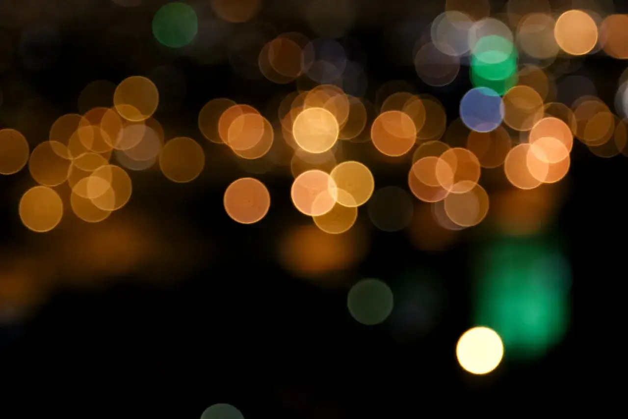 Des lumières douces et floues dans la nuit, comme des bulles dorées et vertes flottant dans le noir. Un effet photo flou qui invite à la rêverie.