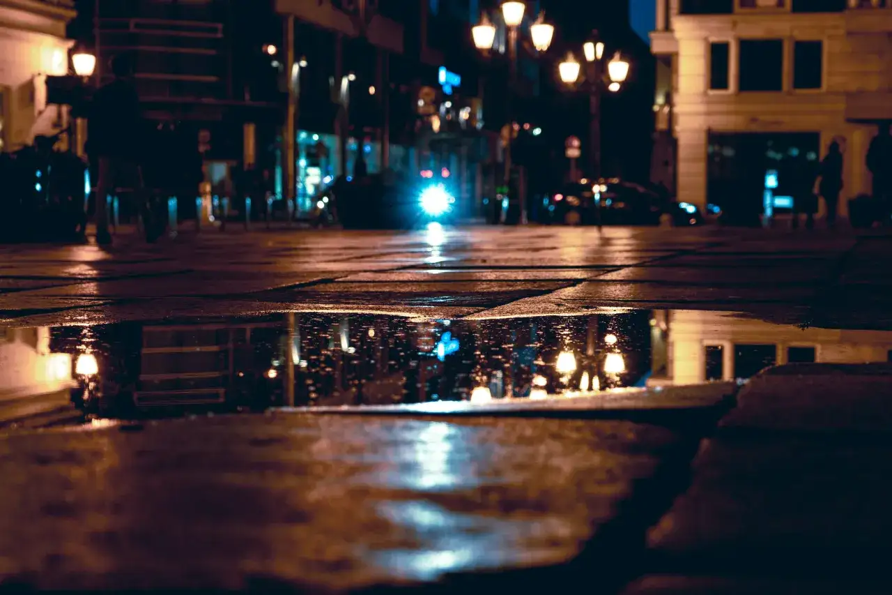 Une rue de ville la nuit, avec des reflets de lumières dans une flaque d'eau. Belles photos sous la pluie, ambiance urbaine et nocturne.