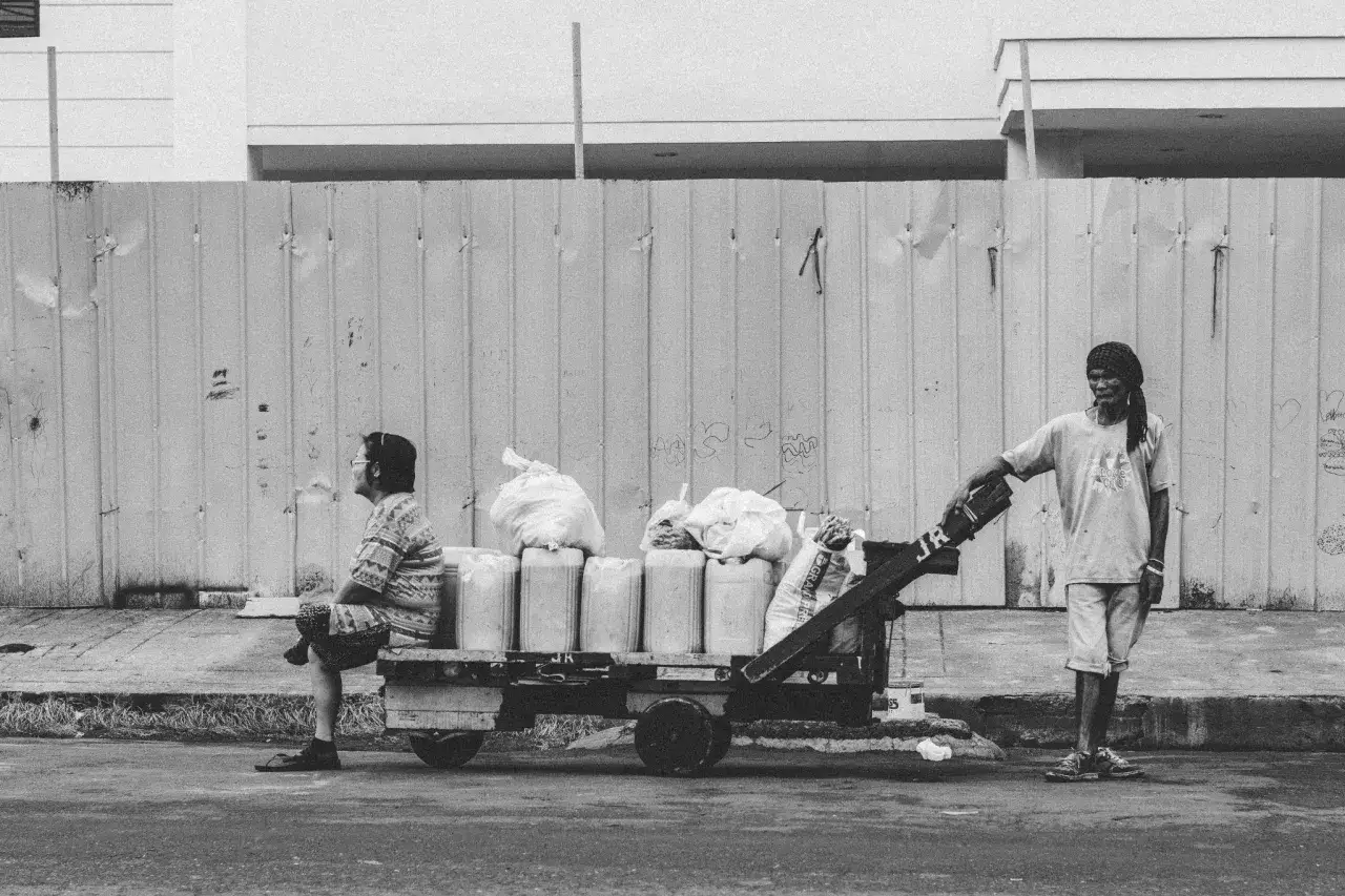 Une femme assise sur une charrette charg&eacute;e de bidons et de sacs, un homme se tient &agrave; c&ocirc;t&eacute;. Une sc&egrave;ne de la vie quotidienne captur&eacute;e dans cette s&eacute;rie photo.