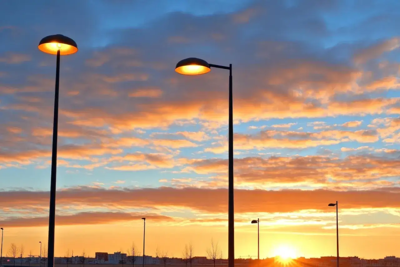 Deux lampadaires s'allument sous un ciel aux couleurs flamboyantes, annonçant le coucher du soleil.
