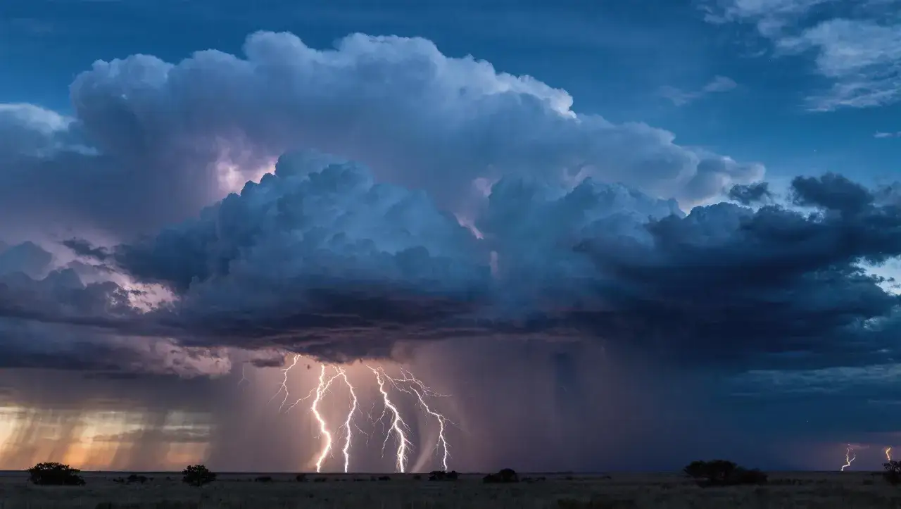 Un spectaculaire photo orage avec des &eacute;clairs illuminant un ciel bleu nuit, des nuages sombres et des rideaux de pluie.