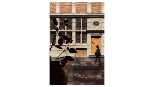 Photographie architecture : une femme passe devant une façade historique aux fenêtres multiples et à la porte en bois.
