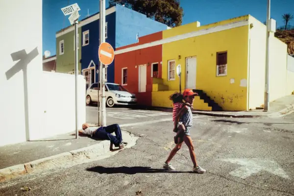 Une jeune fille porte son petit frère dans cette photo de rue colorée. Un homme dort sur le trottoir.