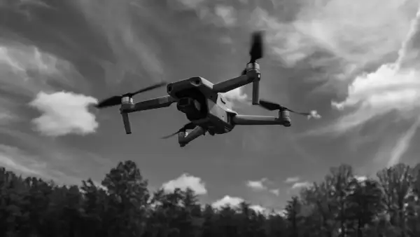Un drone survole une forêt sous un ciel nuageux.