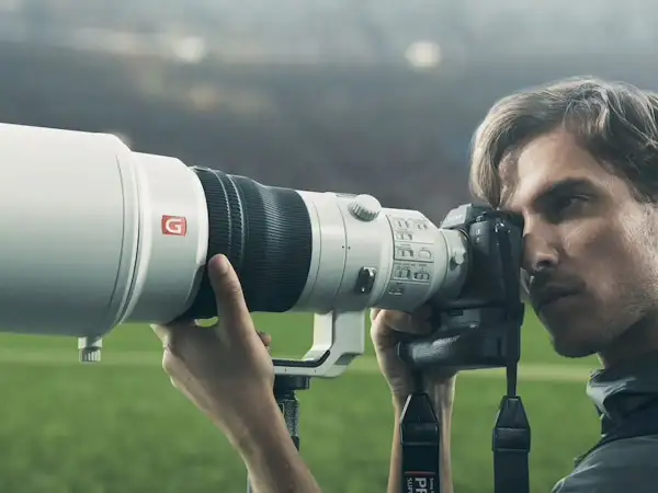 Photographe sportif utilisant un appareil photo Sony a9 II avec un téléobjectif blanc, prêt à capturer l'action sur le terrain.