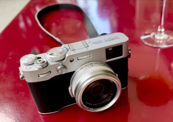 Appareil photo argenté Fujifilm X100VI sur fond rouge vif, prêt pour un test.