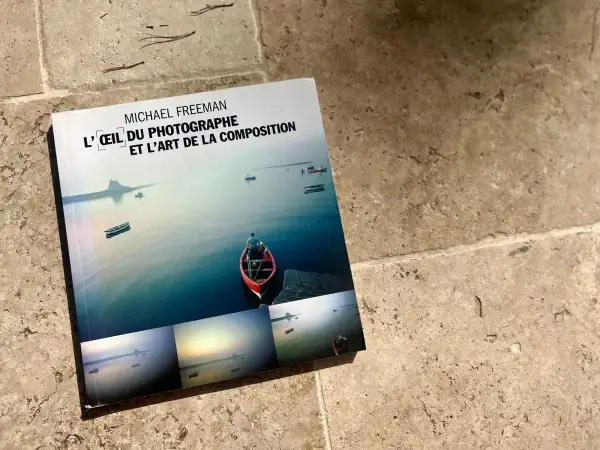 L'œil du photographe et l'art de la composition, un livre de Michael Freeman, présente des paysages marins paisibles avec des bateaux et un îlot lointain.
