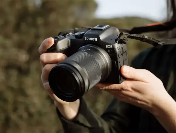 Mains tenant un appareil photo Canon EOS R7 avec un objectif. Prêt à capturer la beauté de la nature.