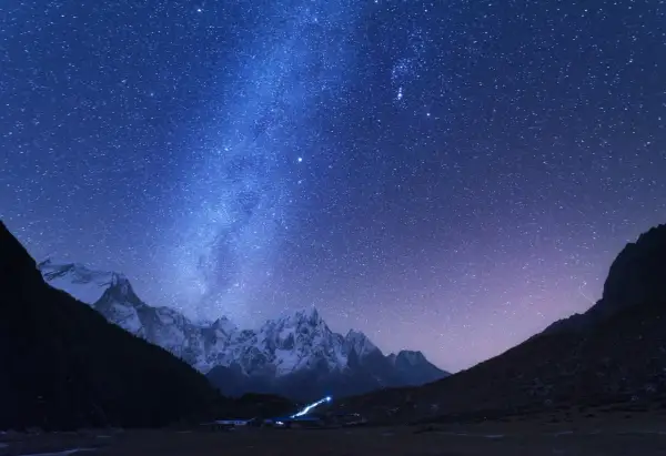 Magnifique photo de nuit. Le ciel étoilé scintille au-dessus de montagnes enneigées et d'un petit village illuminé.