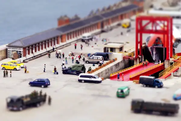 Scène de port avec des véhicules et des personnes, effet tilt shift donnant une impression de maquette.