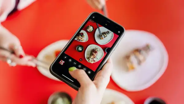 Une main ajuste le paramètre appareil photo Android pour photographier des sushis appétissants sur une table rouge vif.