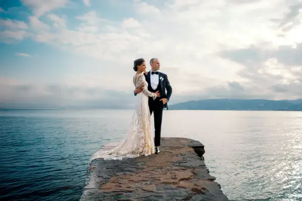 Un couple de jeunes mariés, vêtus de leurs tenues de mariage, pose sur un promontoire rocheux face à la mer. Ces photos de mariage capturent un moment de sérénité.