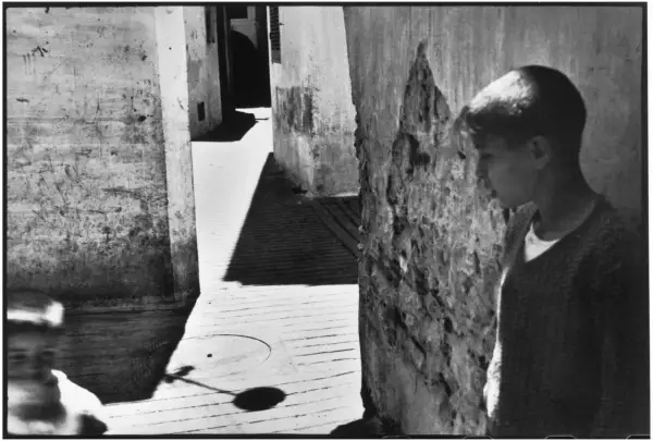 Un jeune garçon se tient dans une ruelle étroite, une ombre projetée sur le sol. Une scène typique des henri cartier bresson photos célèbres.