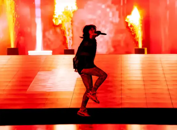 Une artiste chante sur scène, entourée de flammes spectaculaires. Cette photo de concert capture l'énergie d'un spectacle enflammé.