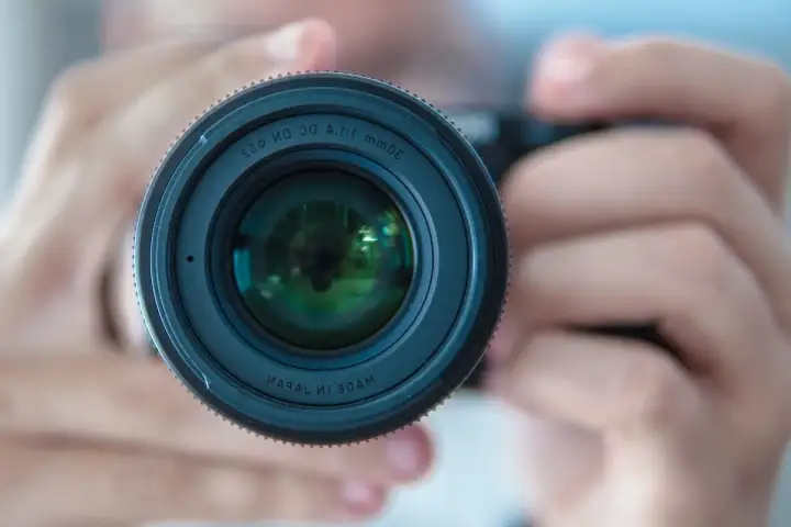 Gros plan sur un objectif d'appareil photo tenu par des mains. La mise au point photographie est parfaite, révélant les reflets verts dans la lentille.